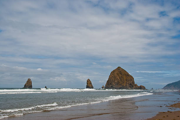 Waves Leading to Haystack Rock The famous Haystack Rock and nearby Needles are basalt monoliths formed some 15-16 million years ago by lava flows emanating from the Blue Mountains and Columbia Basin. Haystack Rock is also one of the most identifiable rock formations on the Pacific Coast. Haystack Rock and the Needles are in Cannon Beach, Oregon, USA. jeff goulden oregon coast stock pictures, royalty-free photos & images