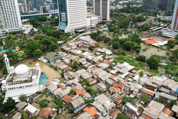The flooded street in a poor residential district in the heart of Jakarta city in Indonesia capital city which show huge inequalities with modern towers surrounding it stock photo