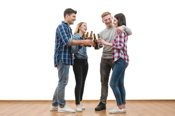 The four happy people hold bottles of beer on a white wall background stock photo