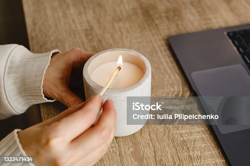 istock The girl lights a candle at her desk at home. A minute of relaxation after working with a laptop. Relaxation and Zen atmosphere 1322471434