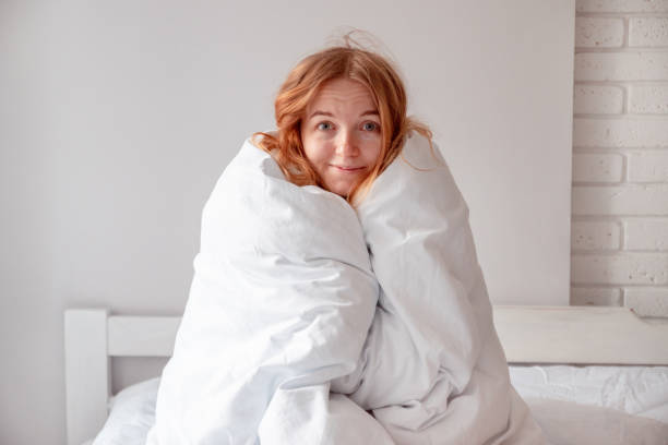 The girl wrapped herself in a blanket The girl wrapped herself in a blanket sitting on the bed looking at the camera blanket stock pictures, royalty-free photos & images