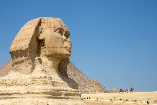 The Great Sphinx of Giza Visitors seem tiny as they pass near the Great Sphinx of Giza, believed to have been created around 2500 BCE for Pharaoh Khafra.  It is among the oldest, largest, and most famous statues in the world. sphinx stock pictures, royalty-free photos & images
