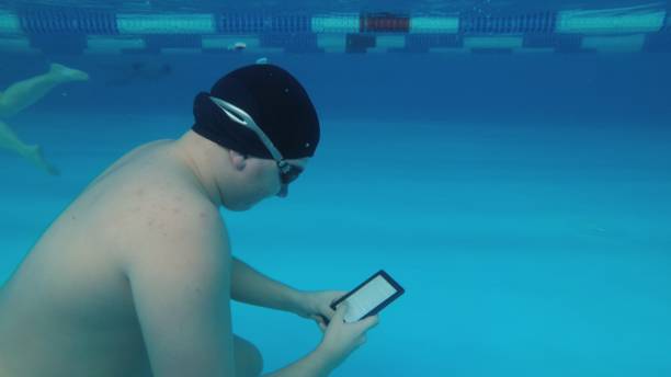 The guy is reading an electronic book underwater. The guy is reading an electronic book underwater. This is a special waterproof electronic device. You can read the text and show signs directly underwater. fat man looks at the phone stock pictures, royalty-free photos & images