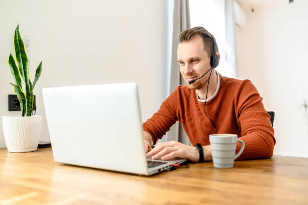 The guy uses hands-free headsets to work from home The guy uses hands-free headsets to work from home. He sits at a table with a laptop and speaks online. Remote work concept hands free device stock pictures, royalty-free photos & images