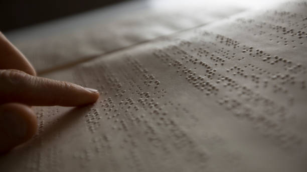 The hand of a blind man reads the text of a braille book. stock photo