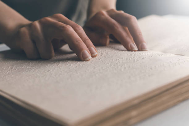 The hand of a blind man reads the text of a braille book. stock photo