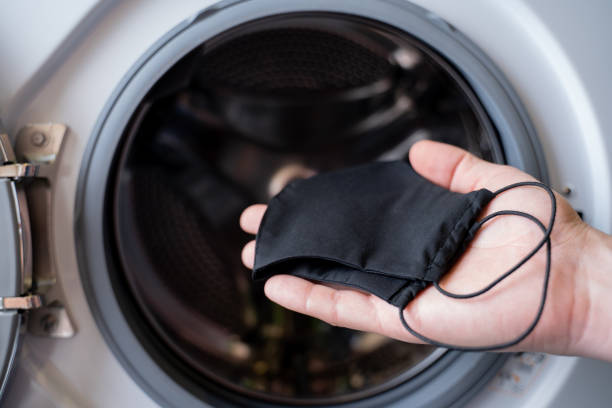 de hand van een mens die een zwart masker in de wasmachine werpt - wassen stockfoto's en -beelden
