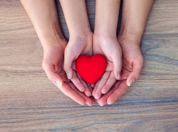 The hands of children and adults in the family have, holding a red heart shape in their hand