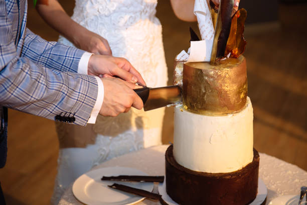 The hands of the bride and groom cut a tiered sweet wedding cake of white gold color. A table with sweets, candy bar stock photo