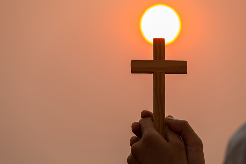The hands of the young women held the cross to pray to God. While the sun is setting Higher religious concepts, the crucifixion of faith, faith in God, prayers, battles and victories of God.