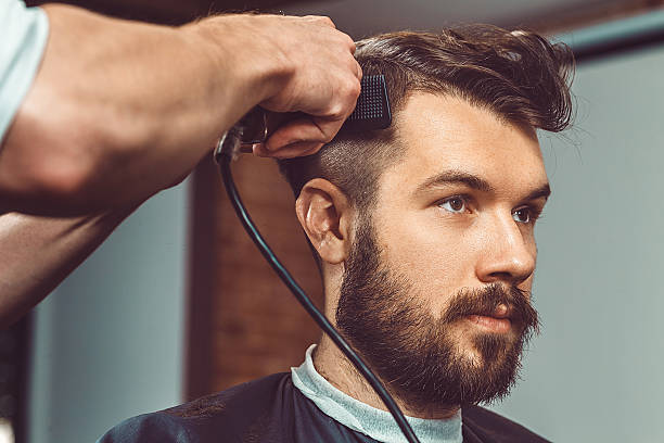 The hands of young barber making haircut to attractive man The hands of young barber making haircut of attractive bearded man in barbershop vintage beauty salon stock pictures, royalty-free photos & images