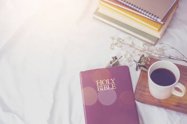 The Holy Bible and a cup of black coffee over blurred book stack on the bed, Christian background morning devotional concept. stock photo
