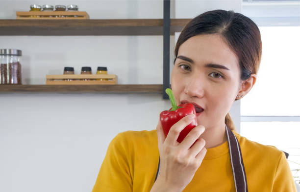 The housewife dressed in an apron bites the delicious red bell pepper. Close up stock photo