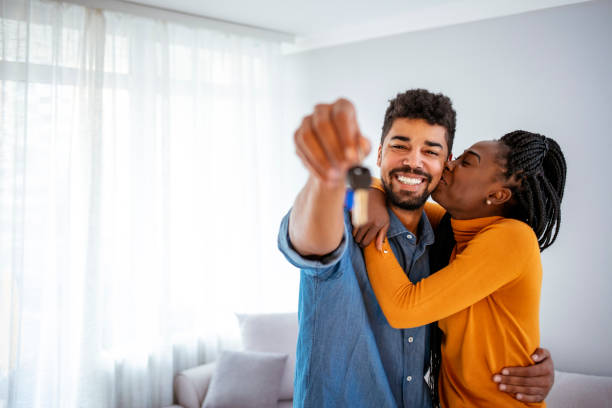 The keys are ours! Young smiling African-American couple showing keys to new home hugging looking at camera. first time home buyer stock pictures, royalty-free photos & images