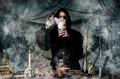 The medieval alchemist make magic ritual at the table in his smoke laboratory. Halloween concept background.