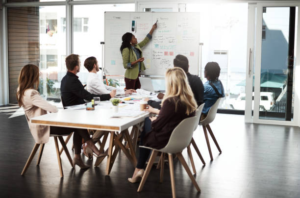 The monthly management meeting has begun Shot of a businesswoman giving a presentation to her colleagues on a whiteboard in a boardroom business strategy stock pictures, royalty-free photos & images