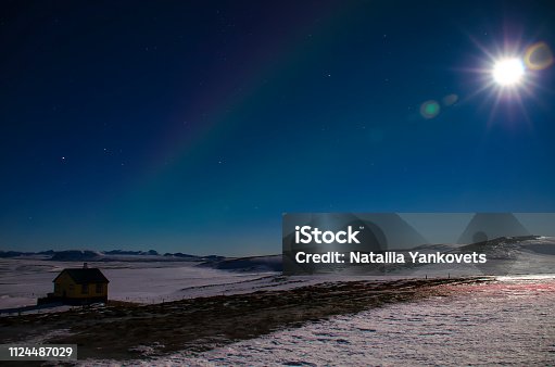 istock The moon with the rays and the northern lights in Iceland s blue winter sky over an Icelandic house that stands on a lava field covered with snow 1124487029