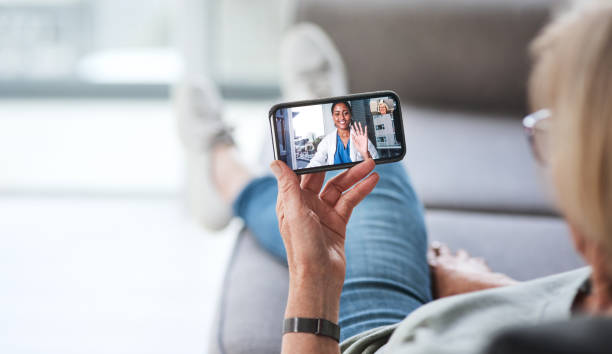The most comfiest consultation ever Shot of a senior woman using a smartphone to make a video call with her doctor on the sofa a home telemedicine stock pictures, royalty-free photos & images