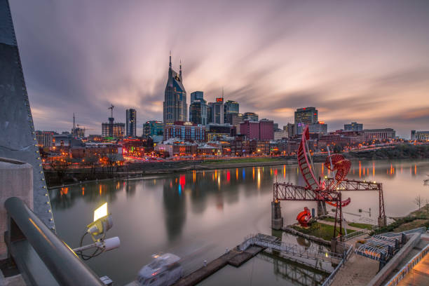 The Nashville skyline reflecting in the Cumberland River as the sun sets and the city lights come on. Nashville, Tennessee - March 23, 2019 : The Nashville skyline reflecting in the Cumberland River as the sun sets and the city lights come on. broadway nashville stock pictures, royalty-free photos & images