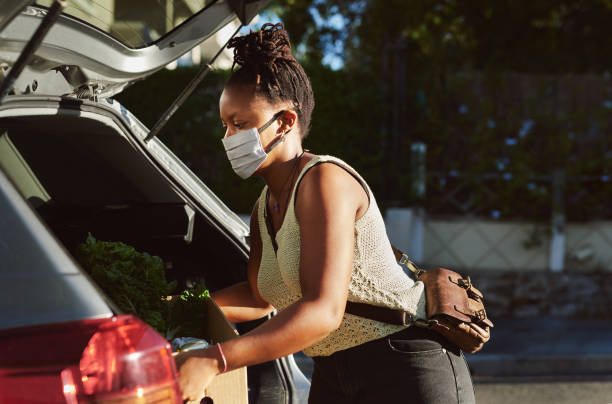 The new reality of retail Shot of a young woman wearing a mask and packing groceries into the trunk of her car south africa covid stock pictures, royalty-free photos & images