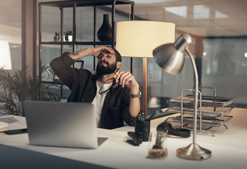 Shot of a young businessman feeling stressed while working late at night in a modern office