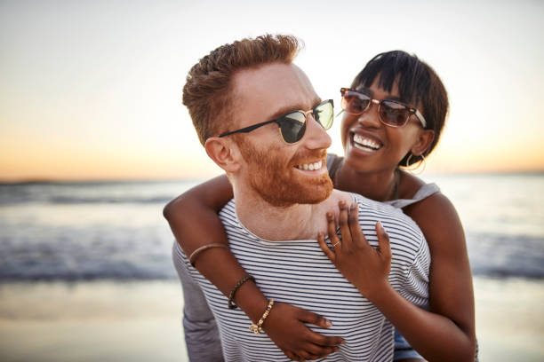 The ocean brings everyone closer together Shot of a happy young couple spending the day at the beach sunglasses stock pictures, royalty-free photos & images