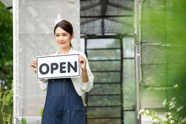 The owner of the tree shop holds a open sign after a long time closed. Cute asian gardener small business open her shop selling small tree for decoration in greenhouse. stock photo