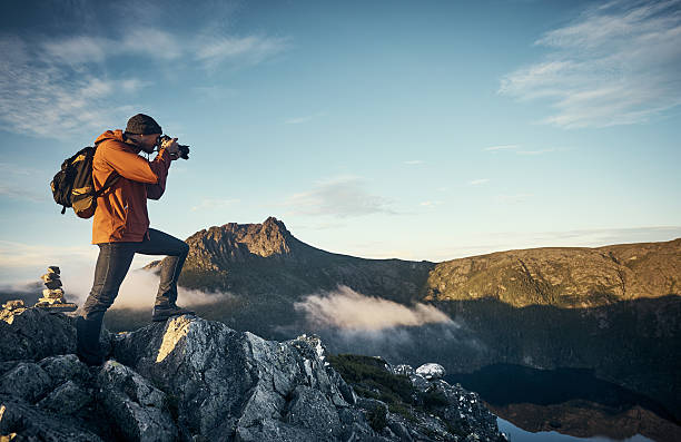 The perfect vantage point Shot of a young man taking photographs while hiking in the mountains scenics nature photos stock pictures, royalty-free photos & images