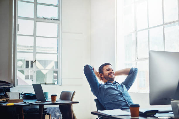 The rewards are in the results Shot of a young businessman relaxing at his work desk contented emotion stock pictures, royalty-free photos & images