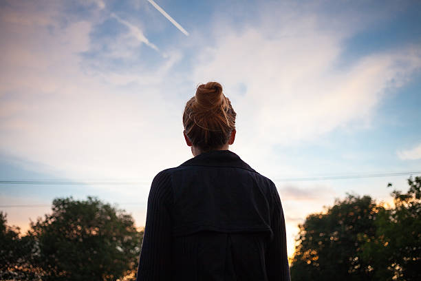 The silhouette of a young woman looking at sunset The silhouette of a young woman looking at sunset in the distance. directly below stock pictures, royalty-free photos & images