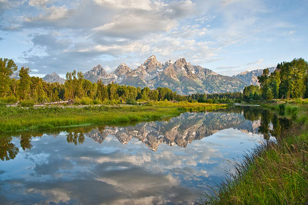 Teton Range Reflected in the Snake River The Snake River flows quietly through the Jackson Hole Valley. In many places the water is so calm and glassy that a perfect reflection of the Teton Range is often seen. This picture of the Tetons at first light was taken from Schwabacher Landing, a very popular place for photographers. Schwabacher Landing is in Grand Teton National Park near Jackson, Wyoming, USA. jeff goulden reflection stock pictures, royalty-free photos & images
