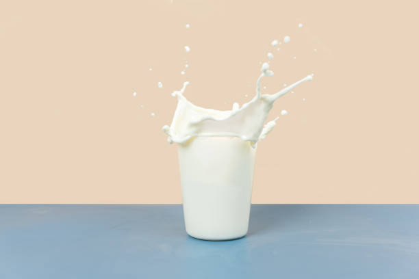 la leche que salpica en la taza es sobre un fondo amarillo y gris - leche fotografías e imágenes de stock
