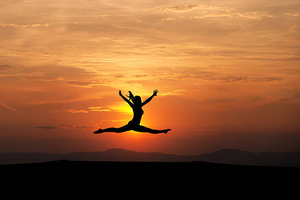 the splits by female gymnast in sunset the splits jump of silhouetted female gymnast in sunset gymnastic silhouette stock pictures, royalty-free photos & images