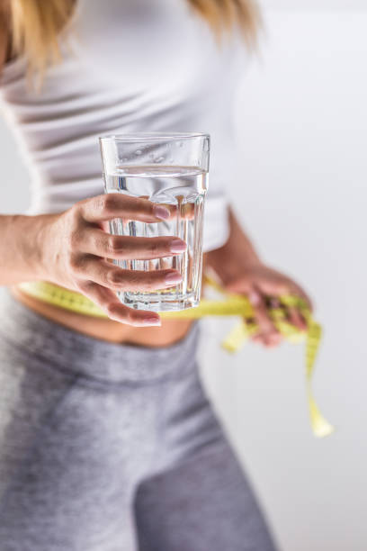 The sport figure of a attractive woman holding cup from pure mineral water and measure tape. The sport figure of a attractive woman holding cup from pure mineral water and measure tape. drinking water weight loss stock pictures, royalty-free photos & images