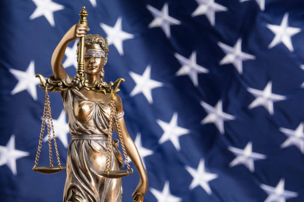 The statue of justice Themis or Justitia, the blindfolded goddess of justice against a flag of the United States of America, as a legal concept stock photo