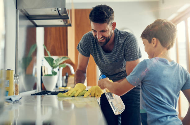 The super disinfecting son and dad duo Shot of a father and son cleaning the kitchen counter together at home spring cleaning stock pictures, royalty-free photos & images