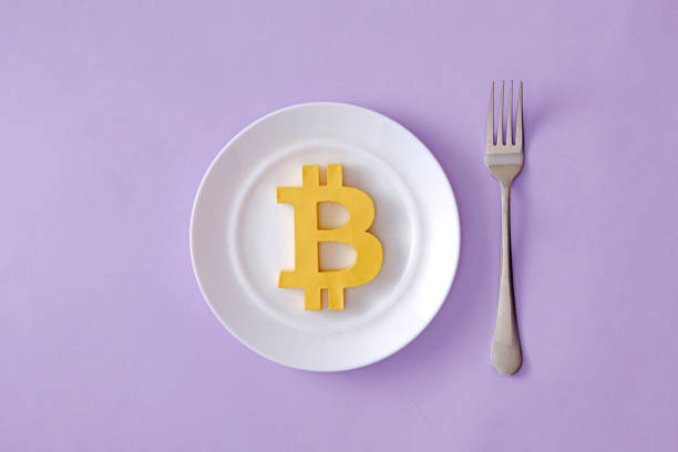 The symbol of the modern digital cryptocurrency Bitcoin in a plate and a fork on the table as food. Minimal concept of economic and financial success or crisis. stock photo