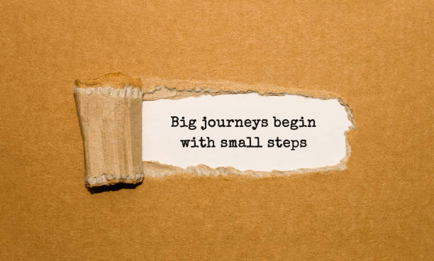 The text Big journeys begin with small steps appearing behind torn brown paper stock photo