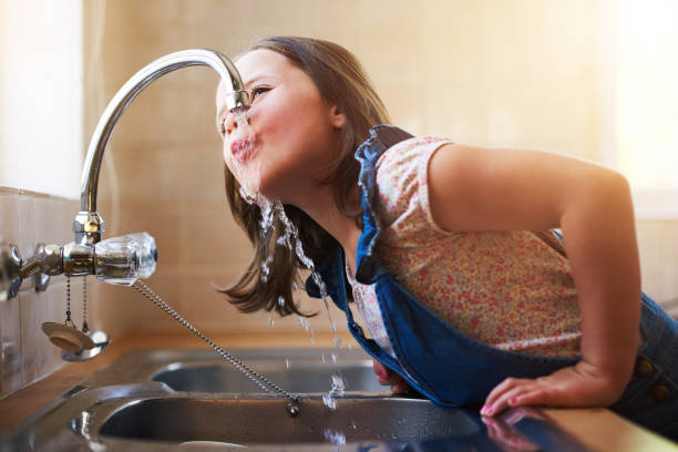 The thirst is real Shot of a little girl drinking water directly from the kitchen tap at home faucet stock pictures, royalty-free photos & images