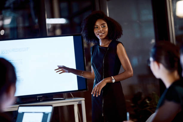 The time for progress is now Shot of a young businesswoman delivering a presentation during a late night meeting at work presentation speech stock pictures, royalty-free photos & images