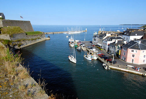 The town quayside, harbour entrance and castle fortified walls viewed from overhead, Sauzon, Belle Isle, Brittany, France. Belle-Île lies off the coast of the Gulf of Morbihan and is Brittany’s largest island. After a turbulent past, which included occupation by the British, the ‘beautiful isle’ is now a magnet for tourists, many of whom arrive by yacht or motorboat. France enjoys many quaint and historic towns and villages both coastal, on its islands and inland with beautiful architecture and historic detail such as stone carving, half timbered building construction and cobbled streets