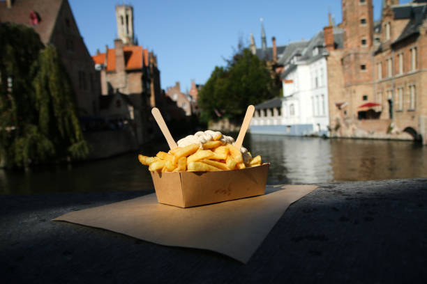 The traditional street food snack, the Belgian Fries The traditional street food snack, the Belgian Fries with pepper sauce pictured on the wall over the channel in Bruges in Belgium. belgian culture stock pictures, royalty-free photos & images
