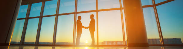 The two businessmen handshake in the office on the bright sun background stock photo