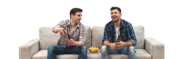 The two men drink a beer with chips on the sofa on a white wall background stock photo