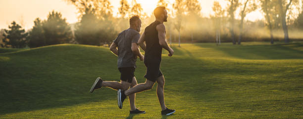 The two sportsmen running on the grass in the park on the sunny background stock photo