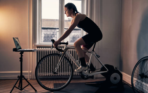 The ultimate way to fitness Shot of a young woman working out on an exercise bike at home peloton stock pictures, royalty-free photos & images