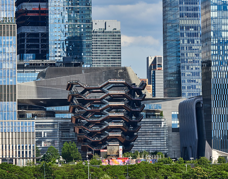 New York, NY - June 23, 2021: The Vessel (2019) in Hudson Yards, Manhattan NYC, as seen from a boat in the Hudson River. Designed by Thomas Heatherwick, it is honeycomb-like structure of 154 flights of stairs, 2,500 steps, and 80 landings for climbing, created at the cost of aprox $200 million.