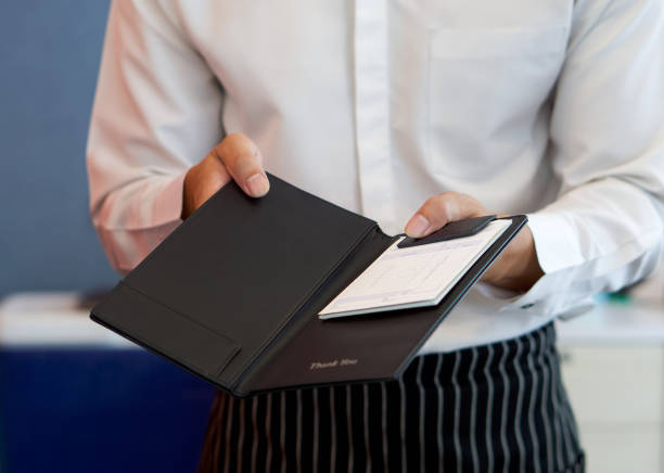 The waiter in a white shirt and apron presents a receipt after calling the bill. stock photo