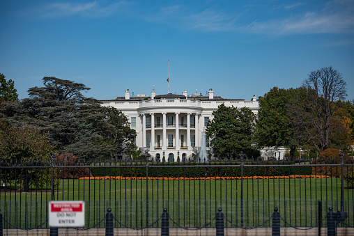 The White House, next to fence on 1600 Pennsylvania Ave.  Home of the President of the United States of America in Washington, DC USA. Blue sky background.