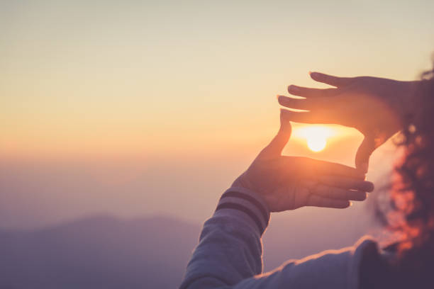 The woman making frame round the sun with her hands in sunrise,copy space,warm retro tone. stock photo